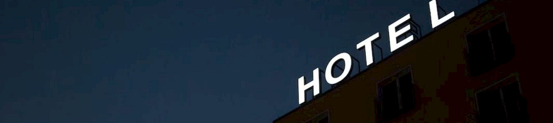 The image shows a building with an illuminated "HOTEL" sign at the top against a dark sky.