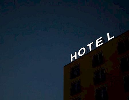 The image shows a building with an illuminated "HOTEL" sign at the top against a dark sky.