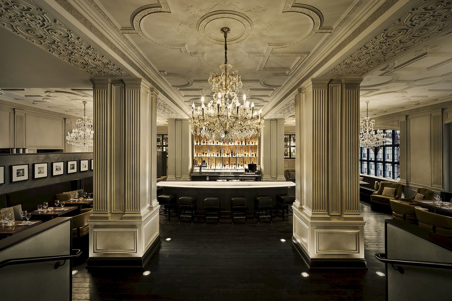 An elegant restaurant interior with ornate chandeliers, long tables, and cozy booths surrounded by intricate architectural details and ambient lighting.