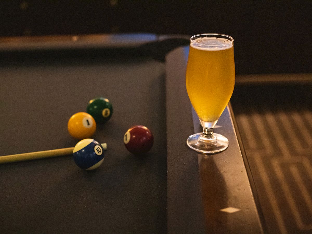 A billiard table featuring a pool cue, balls, and a glass of beer placed on the edge of the table.