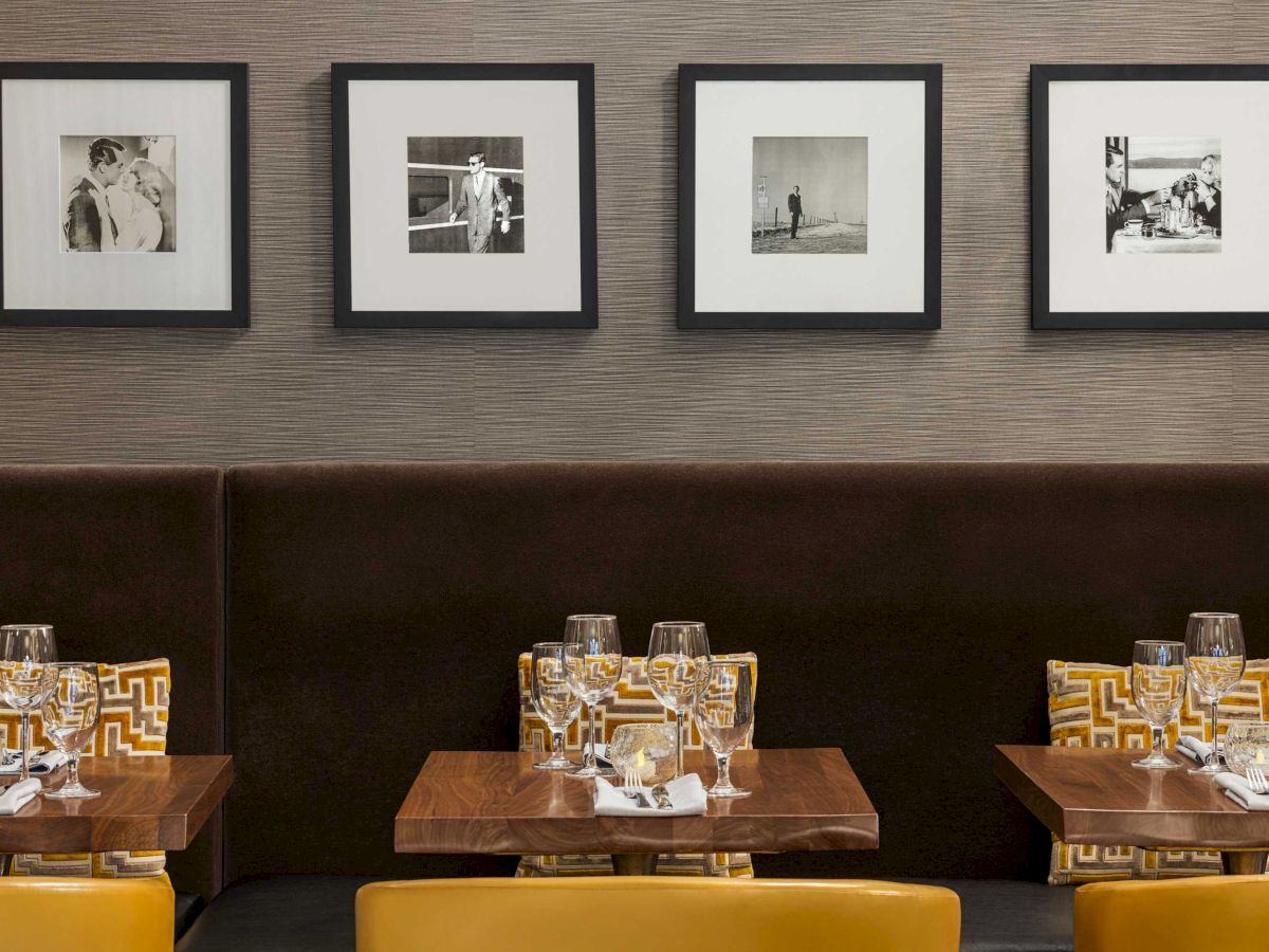 A cozy restaurant interior with framed black-and-white photos on the wall, and wooden tables set with glasses and tableware.