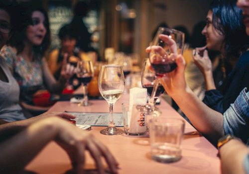 People sitting around a table in a restaurant, enjoying drinks and socializing. Various glasses and a menu are on the table.