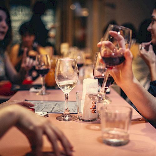 People sitting around a table in a restaurant, enjoying drinks and socializing. Various glasses and a menu are on the table.