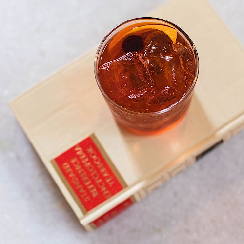 A glass with an iced beverage is placed on top of a closed book, which has a red and white spine label.