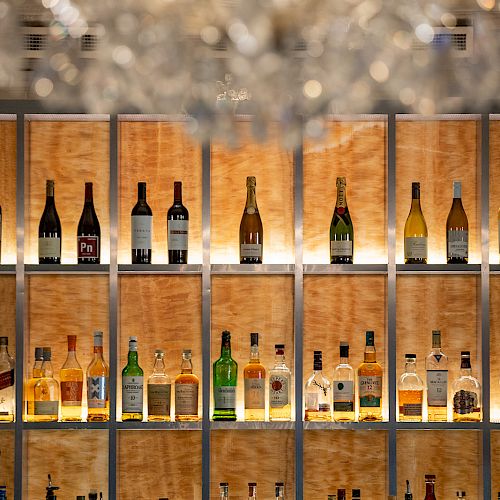 This image shows a well-stocked bar with multiple shelves of assorted liquor bottles, illuminated against a wooden backdrop.